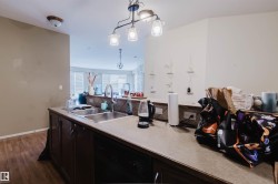Kitchen peninsula featuring a double basin sink with a gooseneck faucet, dark wood cabinetry, and a black built-in dishwasher - 