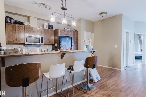 Kitchen featuring wood-finish cabinetry, stainless steel over-the-range microwave, and a breakfast bar with pendant lighting - 323 4831 104A Street, Edmonton, AB 