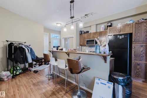 Kitchen area featuring wood-finish flooring, a breakfast bar with seating, recessed and pendant lighting, and a black refrigerator - 323 4831 104A Street, Edmonton, AB 