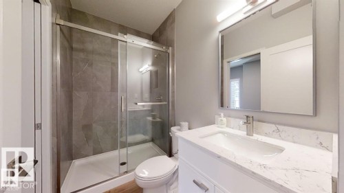 Bathroom featuring a frameless glass shower enclosure with gray tiled walls, a white shower base, and a built-in shower niche - 3918 3A Avenue, Edmonton, AB 