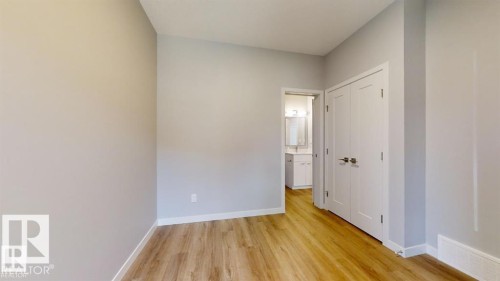 Interior room featuring light wood-finish flooring, light grey painted walls, white baseboards, and a white bi-fold closet door with brushed nickel hardware - 3918 3A Avenue, Edmonton, AB 