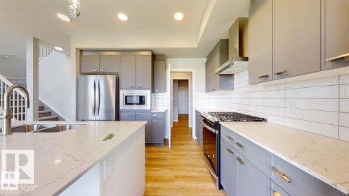 Kitchen featuring an island with an undermount sink, light-toned countertops, grey cabinetry with gold-toned hardware, stainless steel appliances, and wood-finish flooring - 3918 3A Avenue, Edmonton, AB 