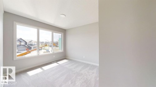 Spacious room featuring a three-panel window, light gray carpet flooring, neutral painted walls, and a recessed ceiling light fixture - 3918 3A Avenue, Edmonton, AB 