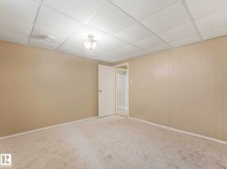 Carpeted room featuring light beige walls, white baseboards, and a paneled drop ceiling with a central flush-mount light fixture - 