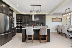 Modern kitchen featuring dark wood cabinetry, stainless steel appliances, a center island with seating, pendant lighting, and light wood-finish flooring - 