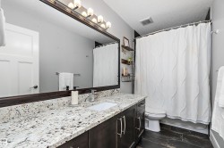 Bathroom featuring a dark wood-finish vanity with dual sinks, a speckled stone countertop, and a large framed mirror with overhead lighting - 