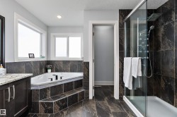 Bathroom featuring a dark tile shower with glass enclosure, a built-in corner soaking tub, and a dark wood vanity with a light countertop - 