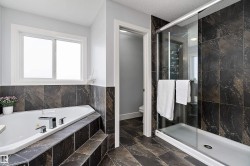 Bathroom featuring a corner soaking tub with deck-mounted fixtures, a separate glass-enclosed shower, and dark stone-look tile flooring - 