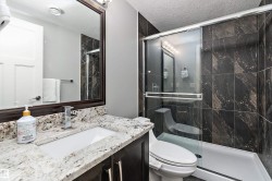 Bathroom featuring a granite countertop vanity with an undermount sink, a chrome single-handle faucet, a framed mirror, and a shower with dark patterned tile and a sliding glass door - 