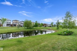 Pond backing property featuring a landscaped green space, a reflective water body, and mature trees - 