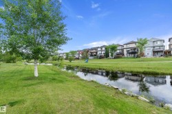 Expansive green space featuring a natural water body, a paved pathway, and mature trees - 