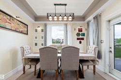 Dining area featuring a tray ceiling with a linear chandelier, light-colored walls, and a glass-paned door - 
