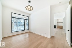 Spacious room with light wood-finish flooring, a contemporary chandelier, a large black-framed window, bright white walls, and a wide entryway - 