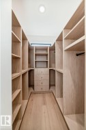 Custom closet system featuring natural wood-finish shelving, built-in drawers with brass hardware, dedicated hanging rods, and recessed ceiling lighting - 