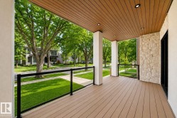 Inviting covered porch with composite decking, recessed lighting, white columns, a stone accent wall, and glass panel railings - 