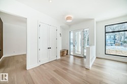 Bright interior space featuring light wood-finish flooring, white walls, and a large black-framed window - 