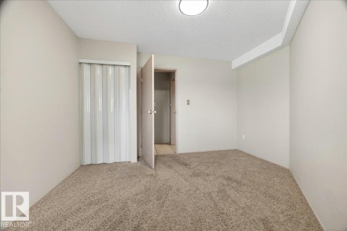 Carpeted room featuring a ceiling-mounted light fixture, light-toned wall paint, and a built-in closet with a white accordion door - 112 6710 158 Avenue, Edmonton, AB 