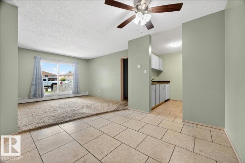 Living space featuring a ceiling fan with light fixture, large sliding glass door, baseboard heating, and an adjacent kitchen area with white cabinetry and dark countertops - 112 6710 158 Avenue, Edmonton, AB 
