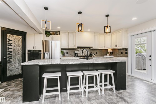 Modern kitchen featuring a large central island with a light-toned countertop, white cabinetry, integrated stainless steel appliances, a gray subway tile backsplash, and wood-finish flooring - 5610 57 Avenue, Beaumont, AB 