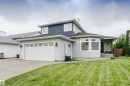 Two-story residence featuring a two-tone exterior with light-colored siding and dark blue shingles, an attached two-car garage with a concrete driveway, a front entry with a bay window, and a sloped front lawn - 5610 57 Avenue, Beaumont, AB 