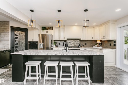 Kitchen featuring a large central island with a light-toned countertop, white cabinetry with dark hardware, stainless steel appliances, a dark subway tile backsplash, and wood-finish flooring - 5610 57 Avenue, Beaumont, AB 