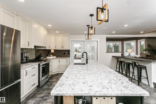 Spacious kitchen featuring a large central island with a sink and black faucet, white shaker-style cabinetry, stainless steel appliances, and wood-finish flooring - 5610 57 Avenue, Beaumont, AB 