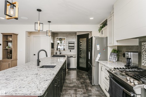 Kitchen featuring an expansive island with a built-in sink, granite countertops, stainless steel appliances, dark wood-finish flooring, and modern pendant lighting - 5610 57 Avenue, Beaumont, AB 