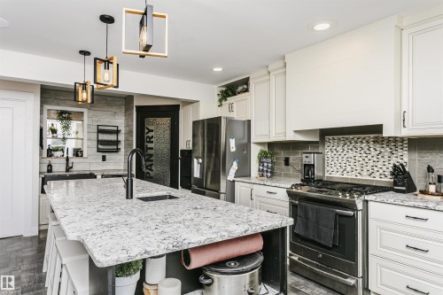 Spacious kitchen featuring a large island with an undermount sink, white cabinetry, stainless steel appliances, a tile backsplash, and decorative pendant lighting - 5610 57 Avenue, Beaumont, AB 