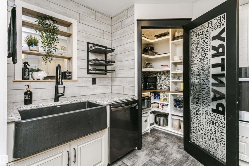 Kitchen featuring a black farmhouse sink with a matte black faucet, granite-style countertops, and white shaker-style cabinetry - 5610 57 Avenue, Beaumont, AB 