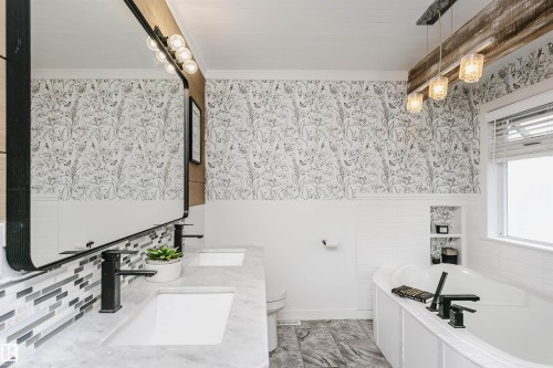 Bathroom featuring a dual vanity with integrated sinks and matte black fixtures, marble-finish countertop, and decorative tile backsplash - 5610 57 Avenue, Beaumont, AB 