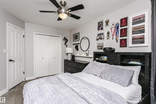 Bedroom featuring wood-finish flooring, a ceiling fan with integrated lighting, a built-in closet with bi-fold doors, and a wall-mounted headboard with shelving - 5610 57 Avenue, Beaumont, AB 