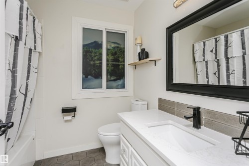 Bathroom featuring a white vanity with an integrated sink, black-framed mirror, and dark hexagonal floor tiles - 5610 57 Avenue, Beaumont, AB 