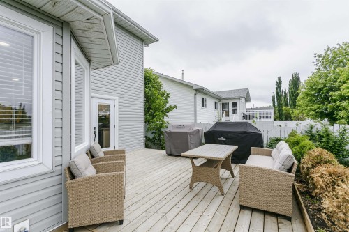 Expansive wood deck with direct access to the interior, featuring horizontal siding exterior, white-framed windows, and mature perimeter landscaping - 5610 57 Avenue, Beaumont, AB 
