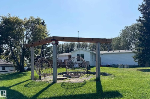 Outdoor entertaining area featuring a wooden pergola structure, two suspended sphere chairs, and a gravel fire pit area - 3054 28 Avenue, Edmonton, AB 