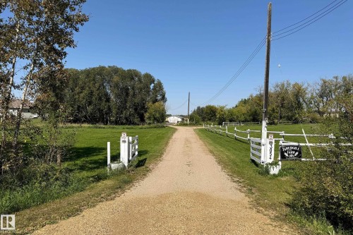 Gravel driveway leading to a distant structure, bordered by green lawns and a white split-rail fence - 3054 28 Avenue, Edmonton, AB 