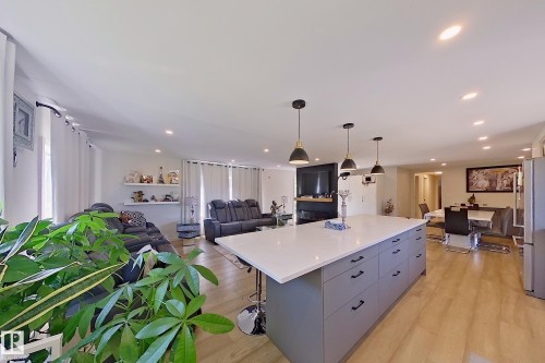 Open-concept living space featuring a central kitchen island with a light-toned countertop, pendant lighting, recessed ceiling lights, wood-finish flooring, and a dining area - 3054 28 Avenue, Edmonton, AB 