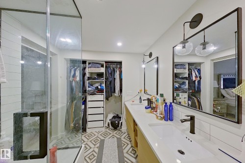 Bathroom featuring a double vanity with undermount sinks, a walk-in shower with glass enclosure, custom closet organization system, geometric floor tiling, and recessed lighting - 3054 28 Avenue, Edmonton, AB 