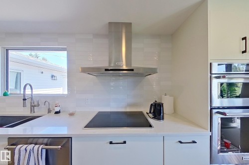 Contemporary kitchen featuring white flat-panel cabinetry, a stainless steel chimney range hood, and a built-in induction cooktop - 3054 28 Avenue, Edmonton, AB 