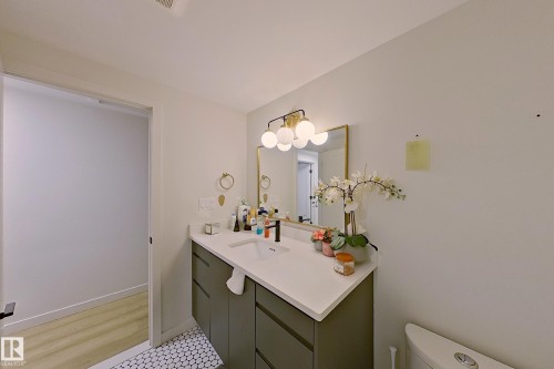 Bathroom featuring a contemporary vanity with a white countertop and integrated sink, a gold-framed mirror, and a modern light fixture with spherical globes - 3054 28 Avenue, Edmonton, AB 