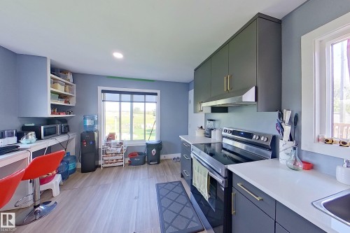 Kitchen featuring wood-finish flooring, dark grey cabinetry with gold-tone hardware, white countertops, built-in shelving, and a stainless steel range with overhead ventilation - 3054 28 Avenue, Edmonton, AB 