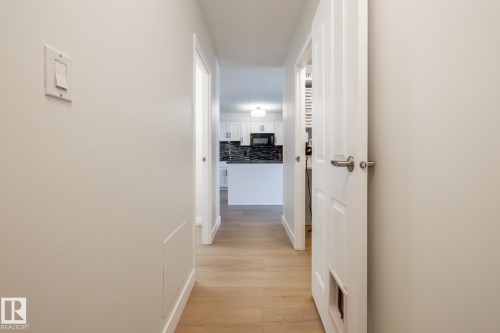 Bright hallway featuring wood-finish flooring, white paneled doors with brushed nickel hardware, and white baseboards - 807 10011 116 Street, Edmonton, AB 