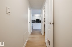 Bright hallway featuring wood-finish flooring, white paneled doors with brushed nickel hardware, and white baseboards - 