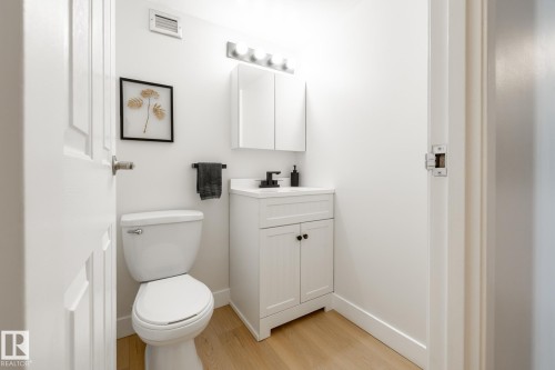 Compact powder room featuring a white single-sink vanity with matte black hardware, a matching medicine cabinet, and wood-finish flooring - 807 10011 116 Street, Edmonton, AB 