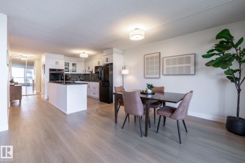 Open-concept living space featuring wood-finish flooring, a white kitchen island with a dark countertop, white shaker-style cabinetry, and built-in black appliances - 807 10011 116 Street, Edmonton, AB 