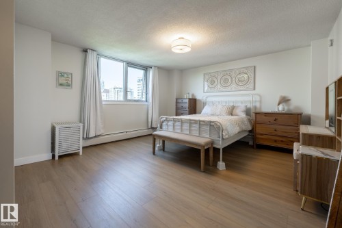 Spacious room featuring wood-finish flooring, a large window with white window treatments, and a flush-mount ceiling light fixture - 807 10011 116 Street, Edmonton, AB 