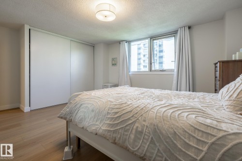 Bedroom featuring light wood-finish flooring, a flush-mount ceiling light fixture, a window with white trim, and a built-in closet with sliding doors - 807 10011 116 Street, Edmonton, AB 