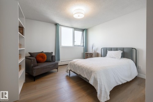 Bright living space featuring wood-finish flooring, a contemporary ceiling light fixture, and a large window with white trim - 807 10011 116 Street, Edmonton, AB 