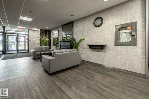 Lobby area featuring wood-finish flooring, a decorative fireplace, and an exposed brick-pattern wall - 807 10011 116 Street, Edmonton, AB 
