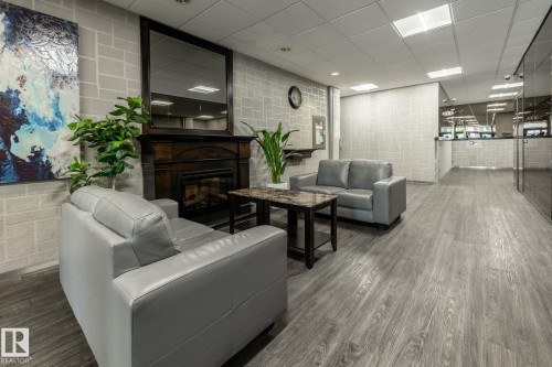 Lobby area featuring wood-finish flooring, light grey brick-patterned walls, a dark wood mantel with a built-in fireplace, and recessed lighting - 807 10011 116 Street, Edmonton, AB 