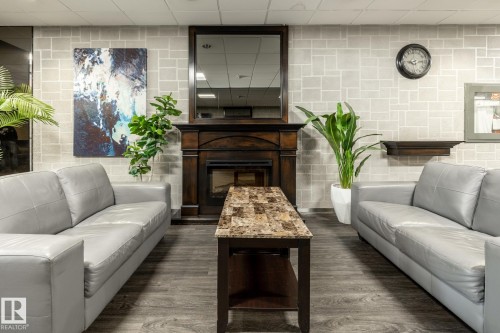 The attractive lobby of Academy Place, featuring a dark wood fireplace with a framed mirror above, light-toned textured wall treatment, and wood-finish flooring - 807 10011 116 Street, Edmonton, AB 